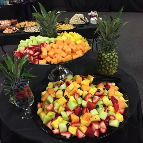 A buffet table with various fruit platters, including pineapples, melon, strawberries, and blueberries.