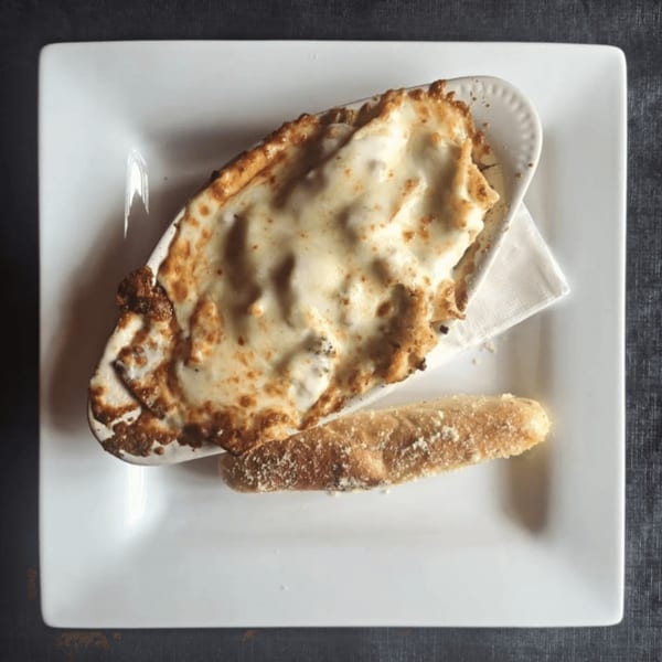 Baked cheesy dip in a white dish with a breadstick on a square white plate.