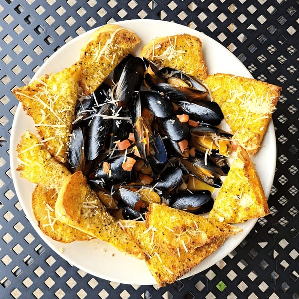 Steamed mussels with diced tomatoes and shredded cheese, surrounded by garlic bread on a white plate.