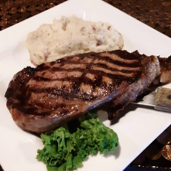 Grilled steak with prominent grill marks, mashed potatoes, and a small garnish of lettuce on a white plate.
