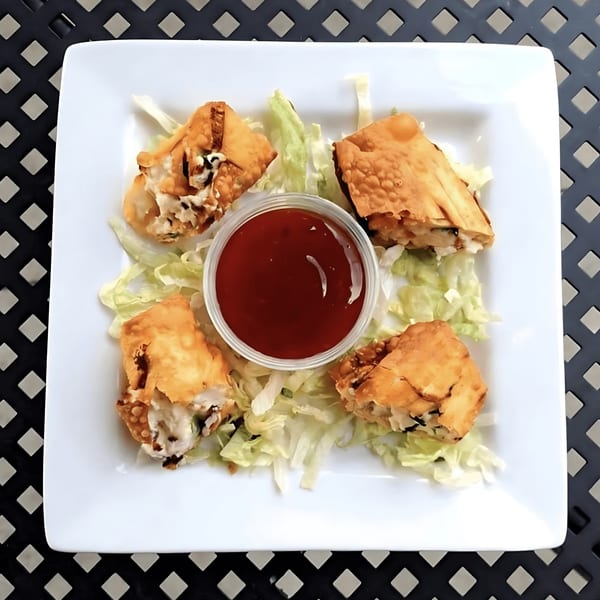 Four crispy egg rolls with shredded lettuce and a side of red dipping sauce on a white plate.