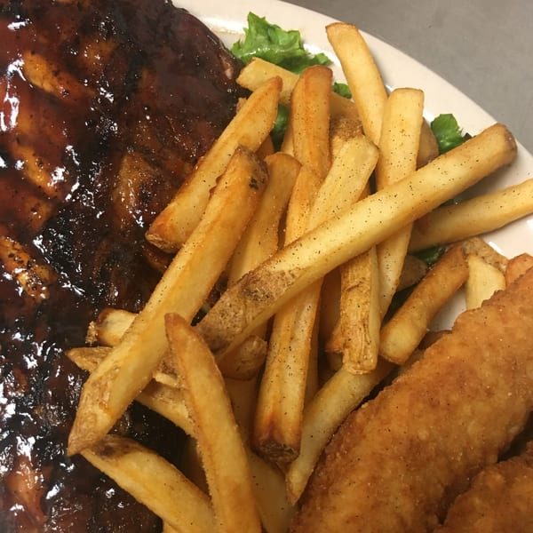 Broadway Grille's BBQ ribs, golden french fries, and crispy chicken tenders on a white plate.