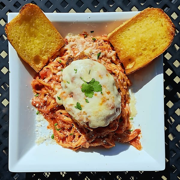 Chicken Parmesan with spaghetti and two slices of garlic bread on a white plate.