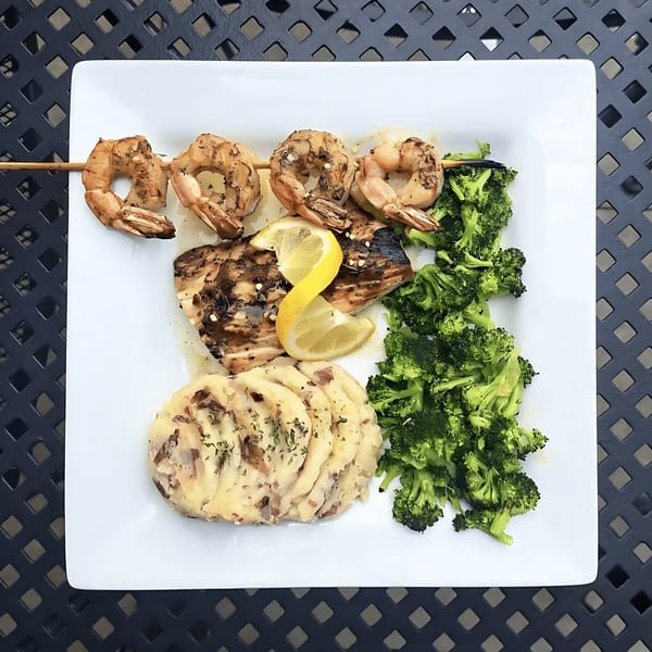 Grilled shrimp skewer, fish, mashed potatoes, and broccoli on a white plate at Broadway Grille.
