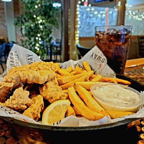 Broadway Grille's fried chicken tenders and fries with dipping sauce and a lemon wedge.
