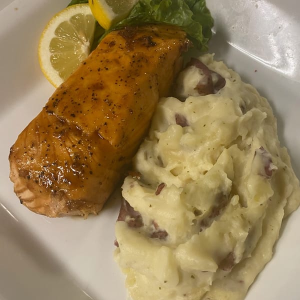 Glazed salmon with mashed potatoes, garnished with lemon slices and lettuce on a white plate.