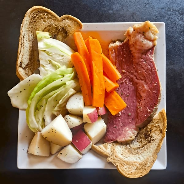 A plate of corned beef, cabbage, carrots, and potatoes, with two slices of bread.